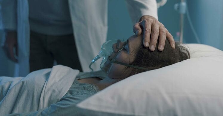 Doctor assisting a hospitalized patient at night and touching her forehead: she is lying in bed with an oxygen mask
