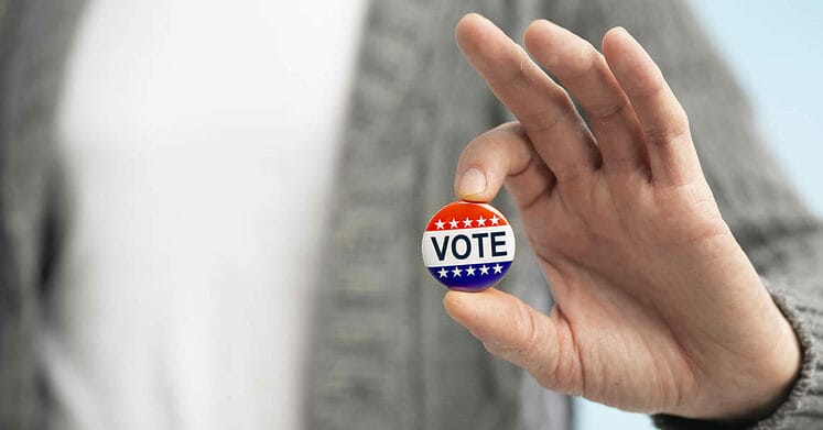 American elections concept 2020. Man with vote pin in hand on blurred background